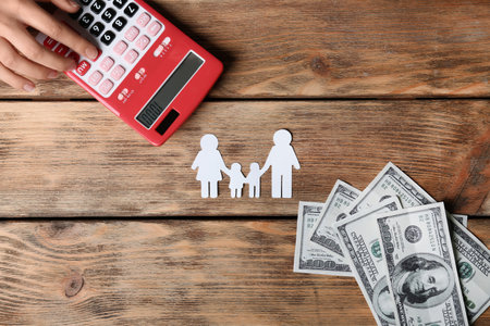 Woman using calculator and paper silhouette of family on wooden background, top view. life insurance conceptの写真素材