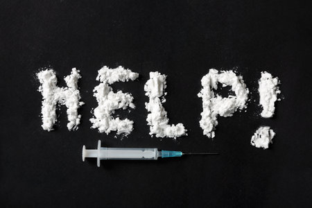 Text Help written with cocaine powder and syringe on black background, top viewの写真素材