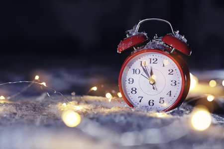 Alarm clock and Christmas lights on white snow outdoors, space for text. midnight count down