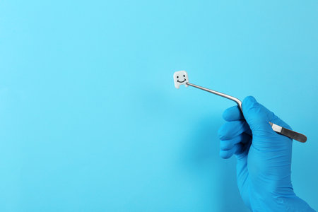 Dentist holding small plastic tooth with tweezers on color background. Space for textの写真素材