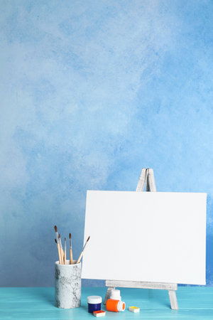 Wooden easel with blank canvas board and painting tools for children on table near color wallの写真素材
