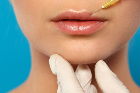 Young woman getting lips injection on color background, closeup. cosmetic surgeryの写真素材