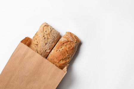 Paper bag with bread loaves on white background, top view. Space for textの写真素材
