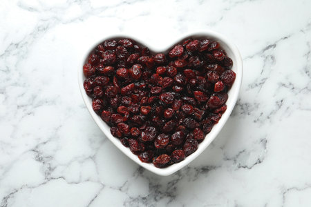 Heart shaped bowl with cranberries on marble table, top view. Dried fruit as a healthy snackの写真素材