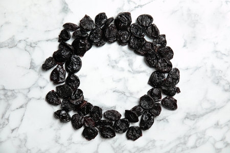 Frame of sweet dried plums on marble background, top view with space for text. Healthy fruits