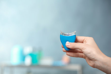 Woman holding teeth whitening device on blurred background. Space for textの写真素材
