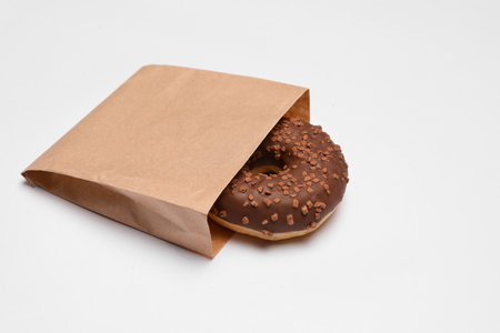Paper bag with chocolate donut on white background. Space for textの写真素材