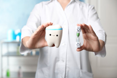Dentist holding model of tooth and sand glass at workplace, closeup view
