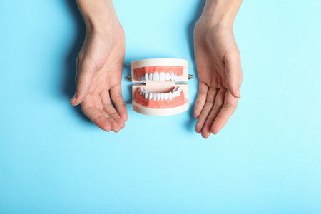 Woman holding hands near educational model of oral cavity with teeth on color background, top view....