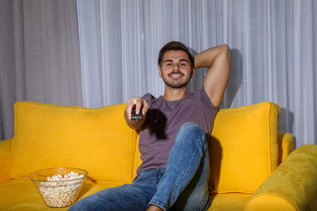 Man changing TV channel with remote control in living roomの写真素材