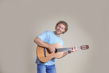 Young man playing acoustic guitar on gray background