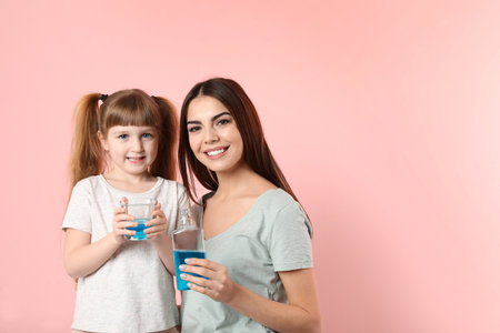 Little girl and her mother with mouthwash on color background, space for text. Teeth and oral careの写真素材