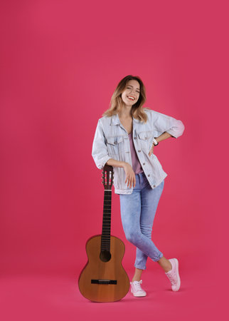 Young woman with acoustic guitar on color backgroundの写真素材