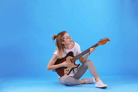 Young woman playing electric guitar on color backgroundの写真素材