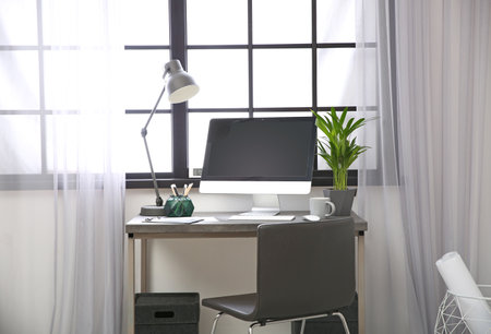 Stylish workplace with computer near window at home office. Space for textの写真素材