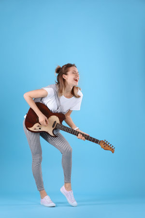 Young woman playing electric guitar on color backgroundの写真素材
