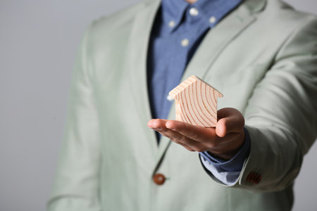 Male agent holding wooden house on gray background, closeup. home insuranceの写真素材