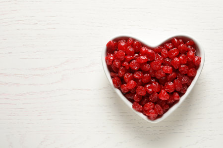 Heart shaped bowl of sweet cherries on wooden background, top view with space for text. Dried fruit as a healthy snackの写真素材
