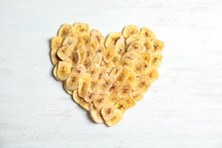 Heart shape made of sweet banana slices on wooden table, top view. Dried fruit as a healthy snackの写真素材