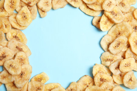 Frame made of sweet banana slices on color background, top view with space for text. Dried fruit as a healthy snackの写真素材