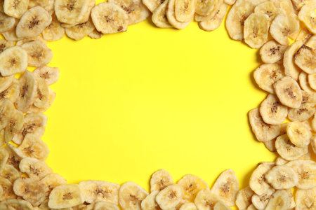 Frame made of sweet banana slices on color background, top view with space for text. Dried fruit as a healthy snackの写真素材