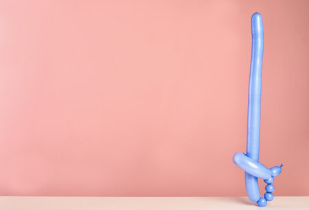 Sword figure made of modeling balloon on table against color background. Space for textの写真素材