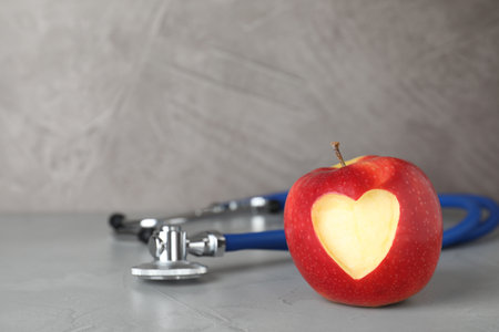 Red apple with carved heart and stethoscope on table. Space for textの写真素材