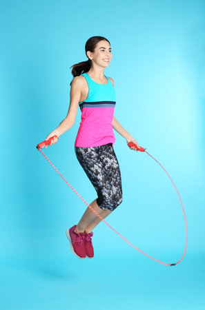 Full length portrait of young sportive woman training with jump rope on color background