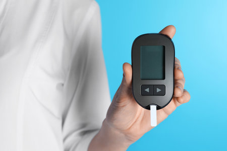 Female doctor holding digital glucometer on color background, closeup. medical objectの写真素材
