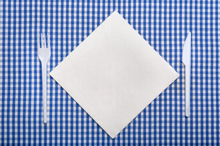 Plastic cutlery and napkin with space for text on plaid fabric, flat lay. Table settingsの写真素材