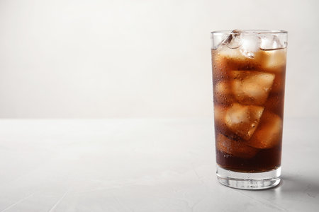 Glass of refreshing cola with ice on light table. Space for textの写真素材