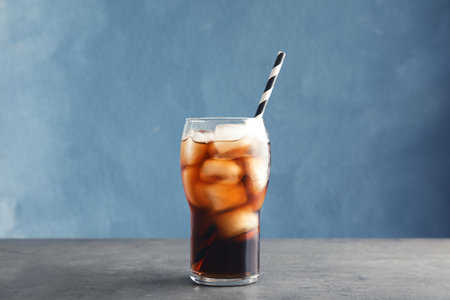 Glass of refreshing cola with ice on table against color backgroundの写真素材