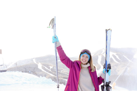 Happy young woman with ski equipment spending winter vacation in mountainsの写真素材