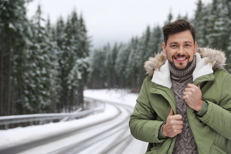 Man in warm clothes near snowy forest, space for text. winter holidays
