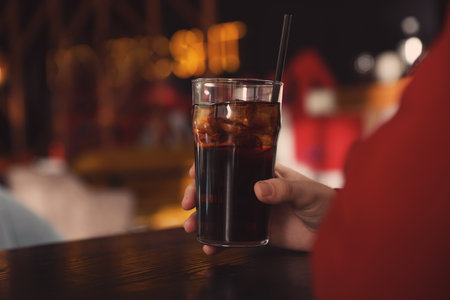 Man holding glass of refreshing cola at table indoors, closeup. Space for textの写真素材