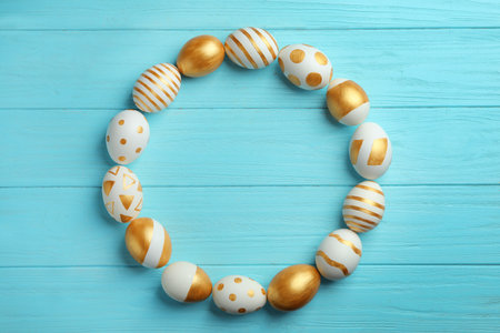 Frame made of traditional Easter eggs decorated with golden paint on wooden background, top view. Space for textの写真素材