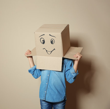 Cute little child wearing cardboard box with smiling face on color backgroundの写真素材