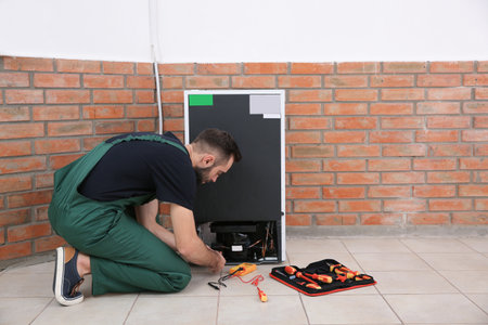 Male technician in uniform repairing refrigerator indoors. Space for textの写真素材