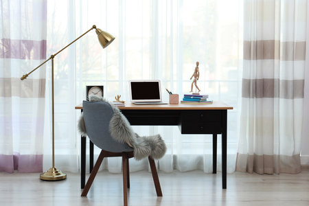 Stylish workplace interior with laptop on table near window. Space for textの写真素材