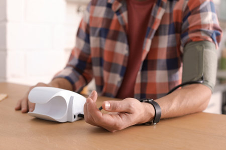 Man checking blood pressure with sphygmomanometer at table indoors, closeup. cardiology concept