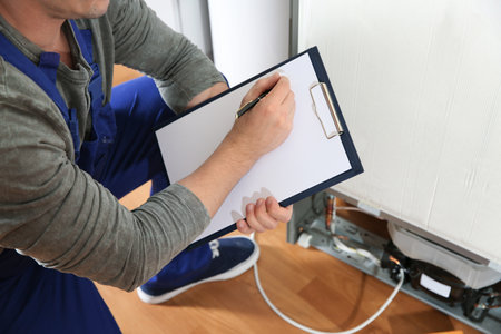 Male technician with clipboard near broken refrigerator indoors, closeupの写真素材
