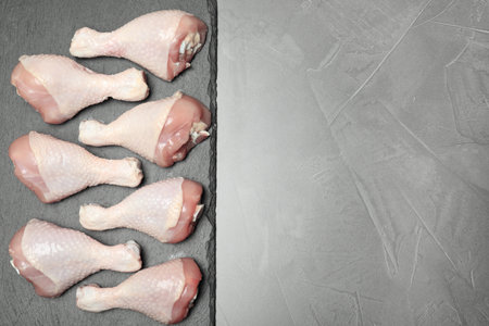 Slate plate with raw chicken drumsticks and space for text on gray background, top view. fresh meatの写真素材
