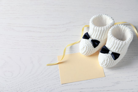 Handmade baby booties and empty greeting card on wooden background. Space for textの写真素材