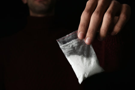 Drug dealer holding bag with cocaine on black background, closeup. Space for textの写真素材