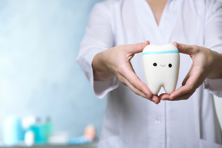 Dentist holding model of tooth with cute face in clinic, closeup view. Space for text