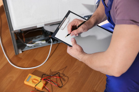 Male technician examining broken refrigerator indoors, closeupの写真素材