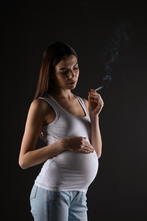 Pregnant woman smoking cigarette on black backgroundの写真素材