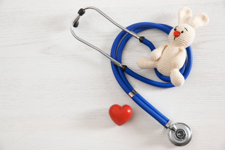 Toy bunny, stethoscope, heart and space for text on white wooden background, top view. children's doctorの写真素材