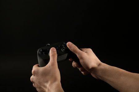 Man holding video game controller on black background, closeup
