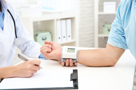 Doctor checking mature man's pulse with medical device in hospital, closeupの写真素材